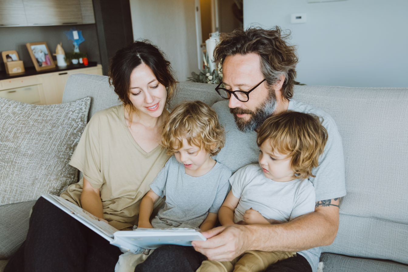 Family of four on a couch looking at a photo album, representing private and secure photo storage and sharing with Tresorit Family.